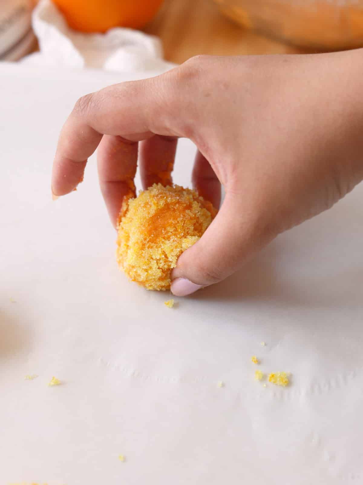 Plopping an sugar cookie dough ball rolled in orange zest onto lined baking sheet.