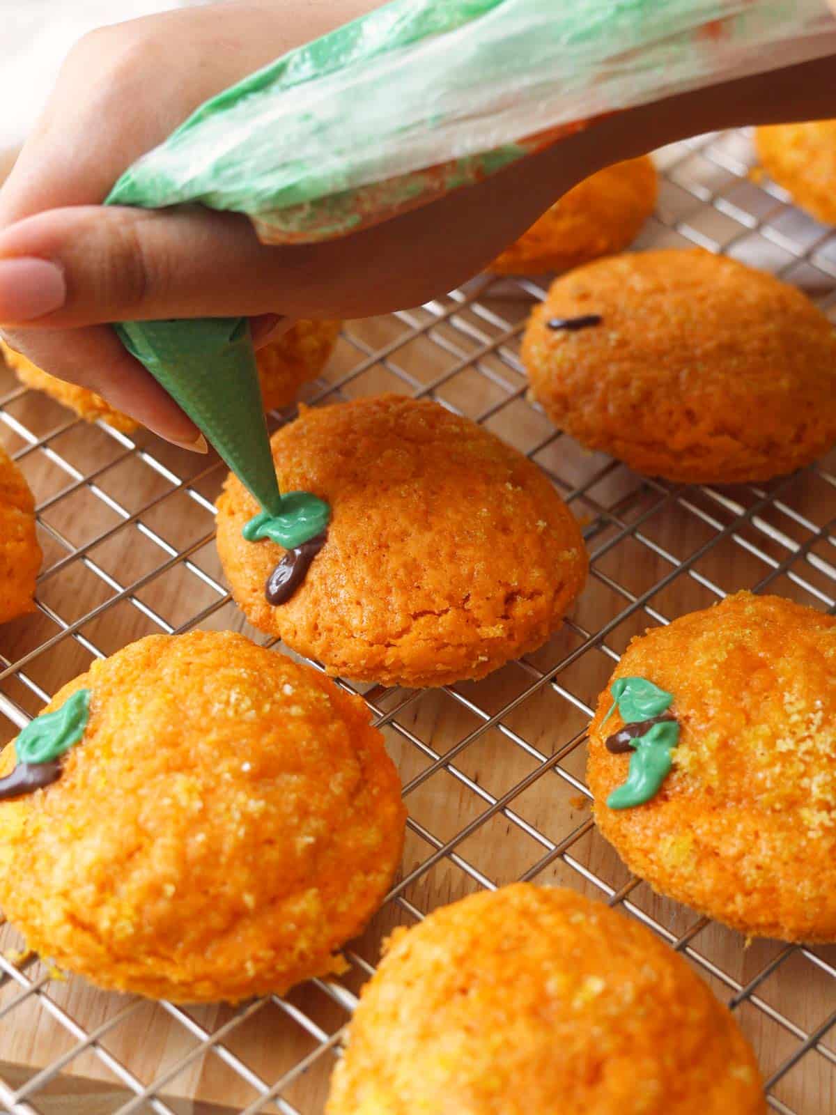 Decorating orange cookies as oranges by using green-dyed white chocolate to draw on leaves.