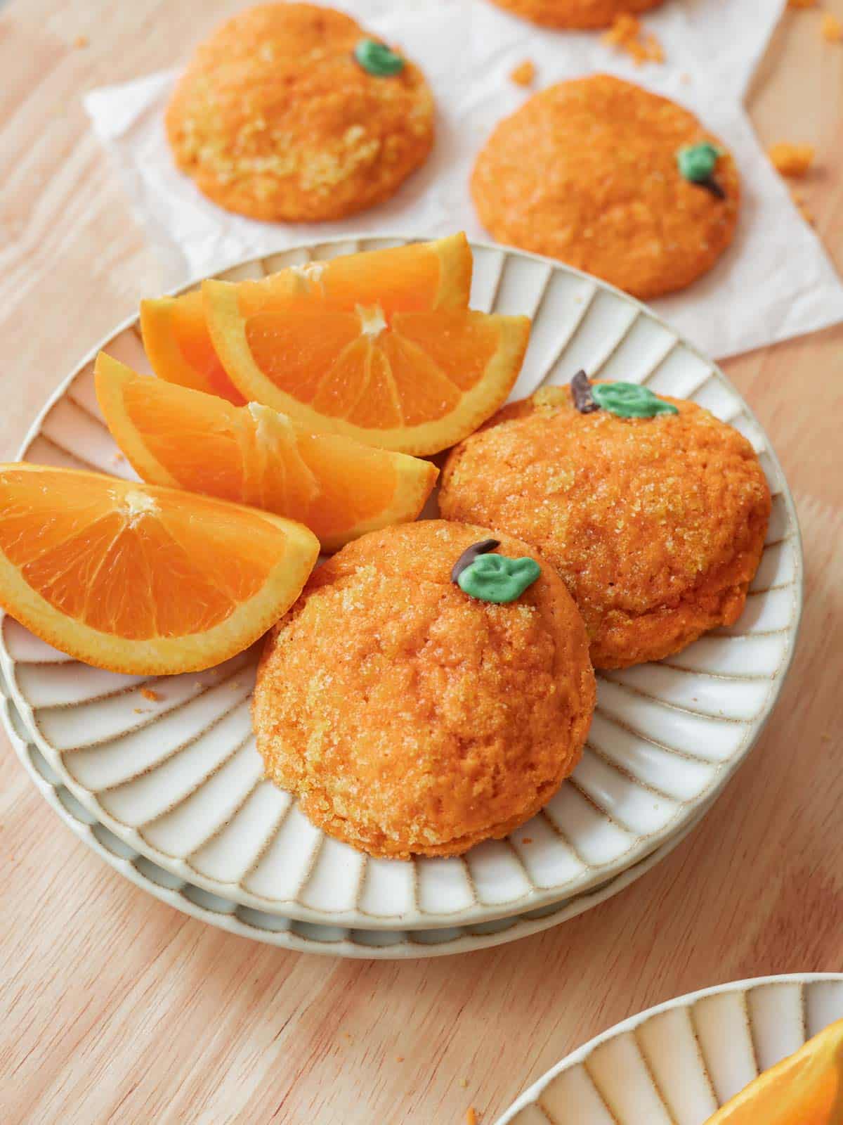 Orange cookies on a plate with freshly cut orange slices.