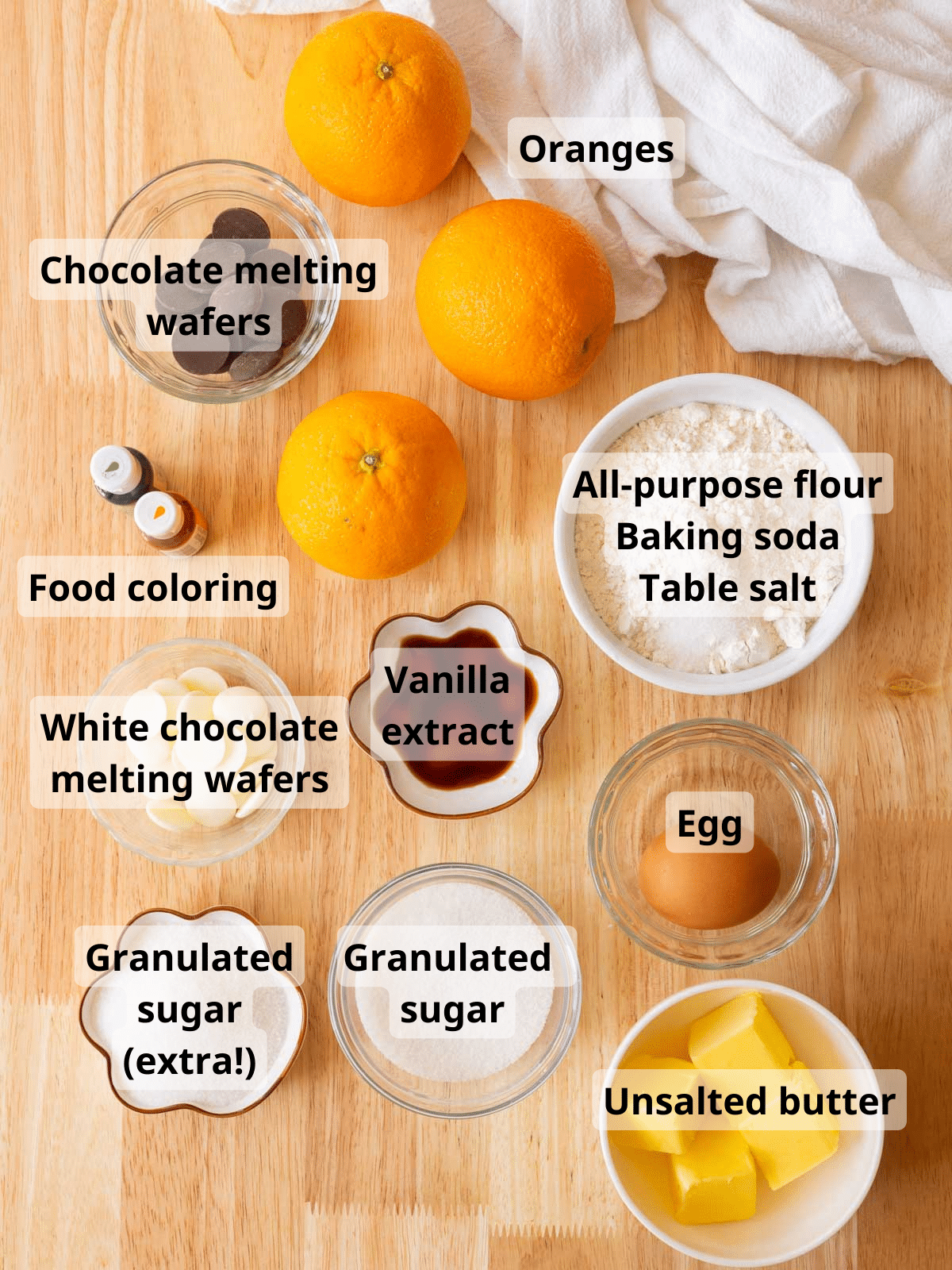 Orange sugar cookie ingredients on a wooden backdrop, all labeled.