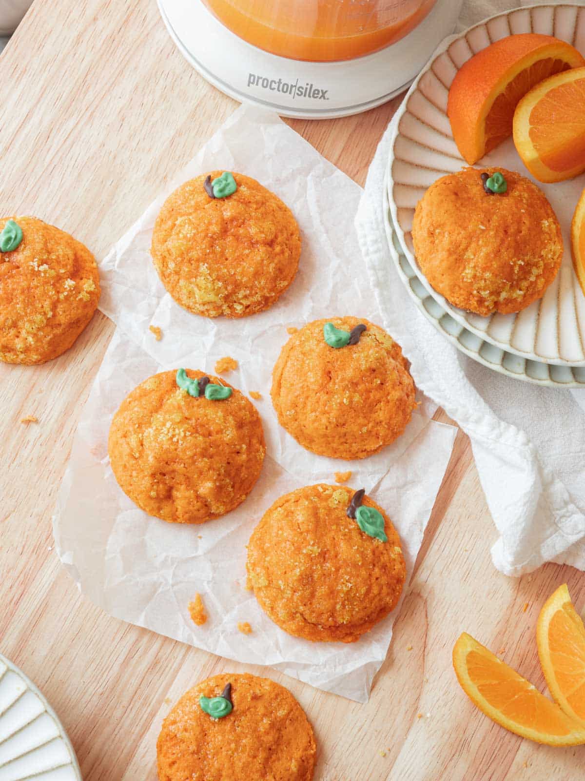 Cute orange sugar cookies decorated as oranges on a light wooden backdrop surrounded cut oranges.