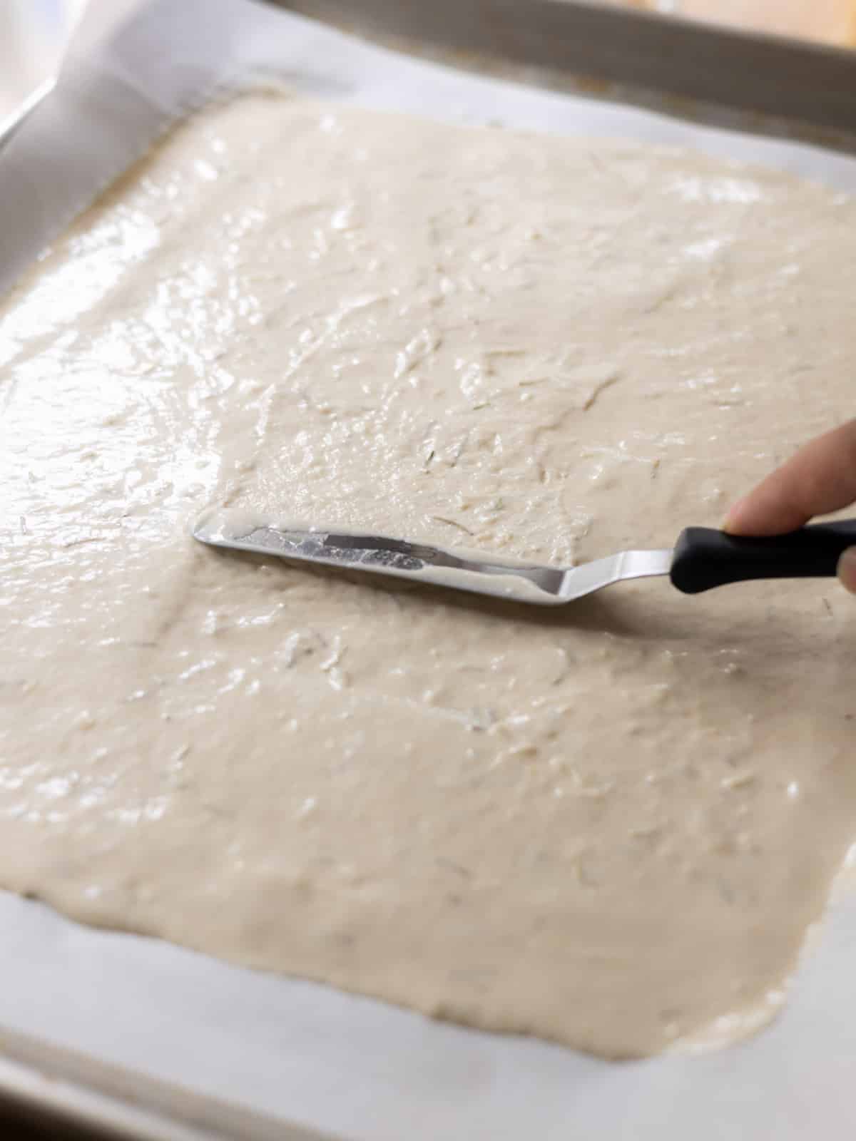 Spreading sourdough discard cracker batter on lined baking tray.