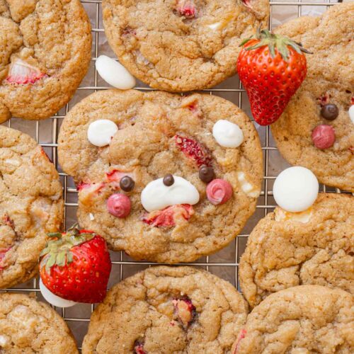 Strawberry cookies on a wire rack, surrounded by white chocolate and fresh strawberries.