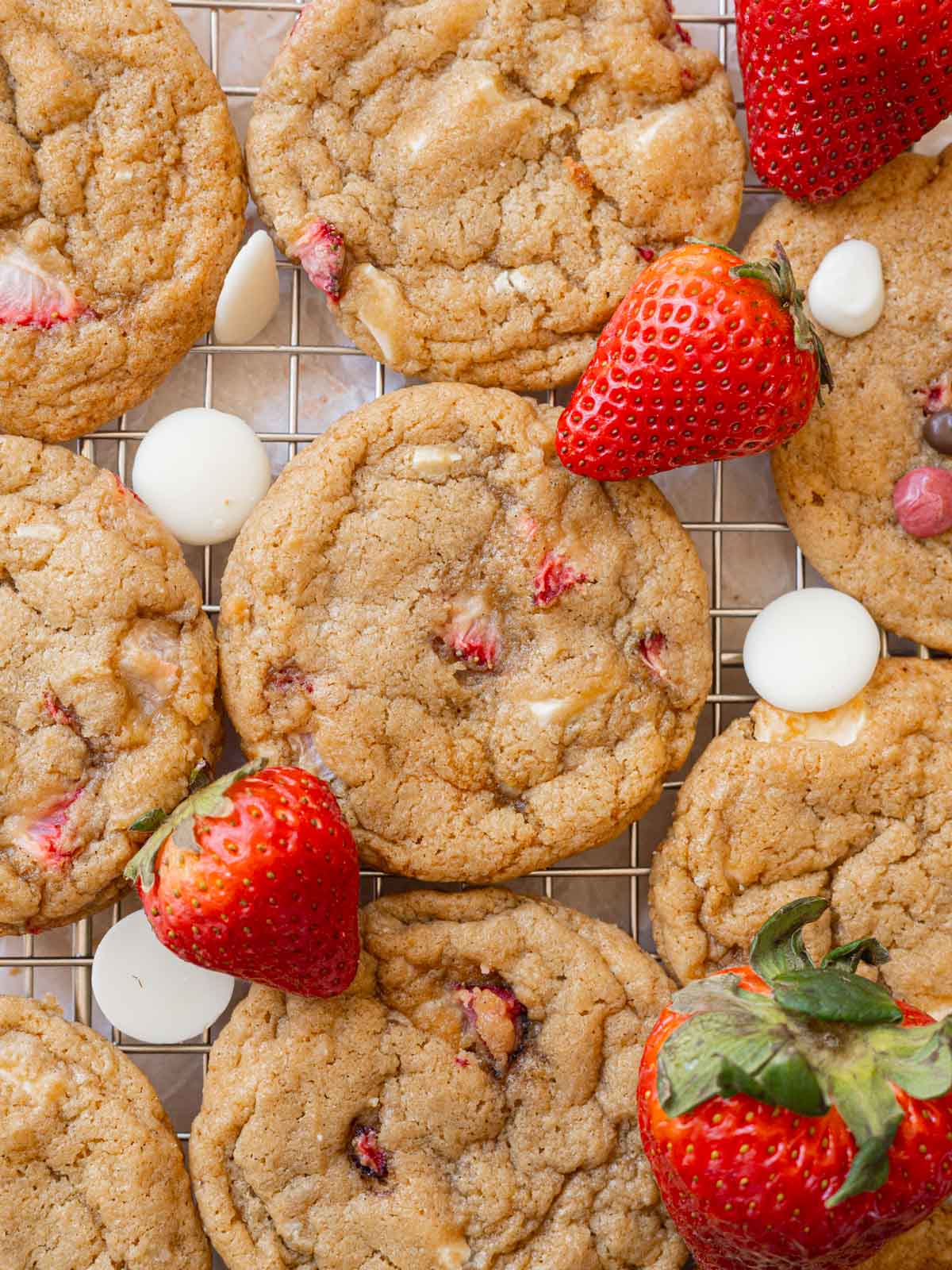 Strawberry cookies on a wire rack, surrounded by white chocolate and fresh strawberries.