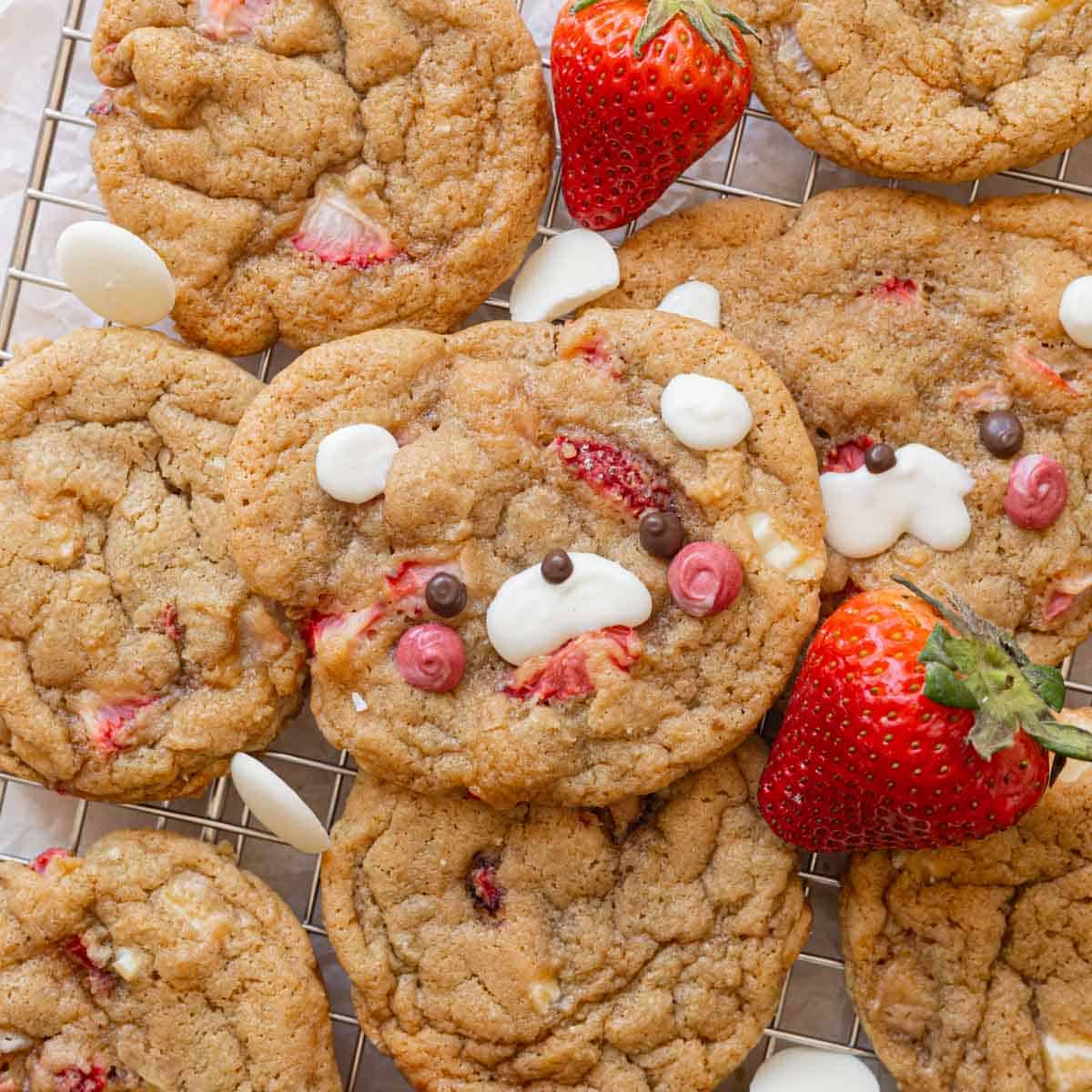 Strawberry cookies on a wire rack, surrounded by white chocolate and fresh strawberries.