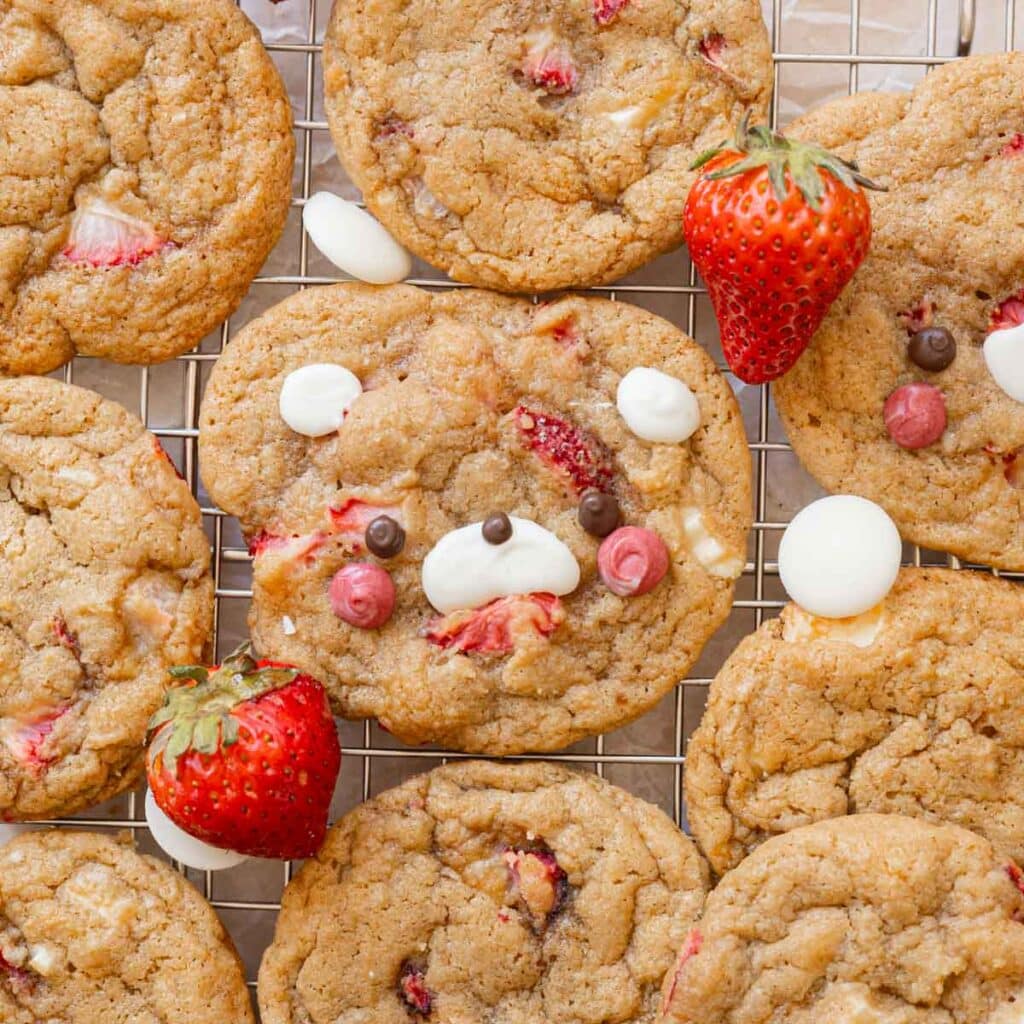 Strawberry cookies on a wire rack, surrounded by white chocolate and fresh strawberries.