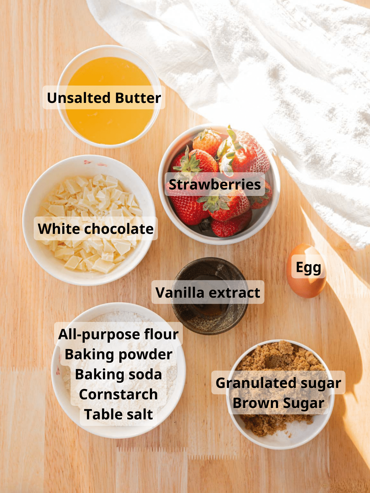 Strawberry cookie ingredients laid out on a wooden backdrop, all labeled.