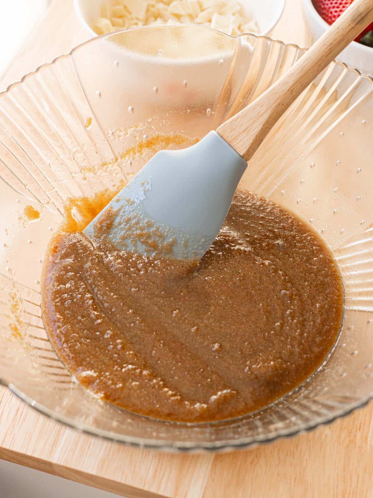 Glass mixing bowl with melted butter and sugars stirred together.