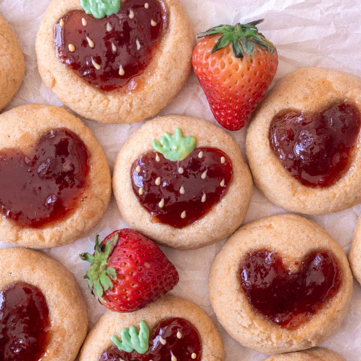 Strawberry thumbprint cookies on parchment paper, with strawberry filling decorated with chocolate to look like strawberries!