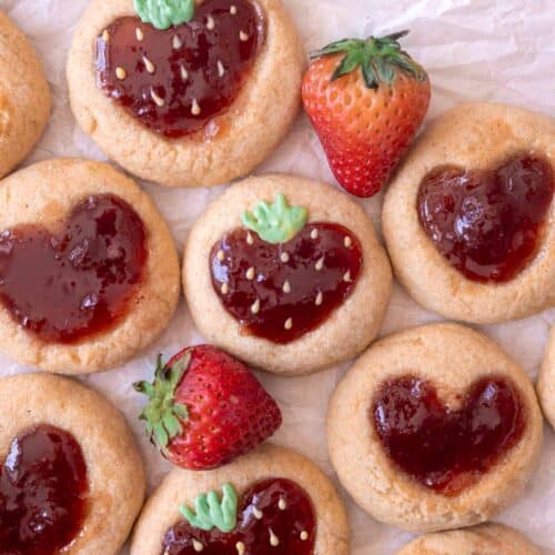 Strawberry thumbprint cookies on parchment paper, with strawberry filling decorated with chocolate to look like strawberries!