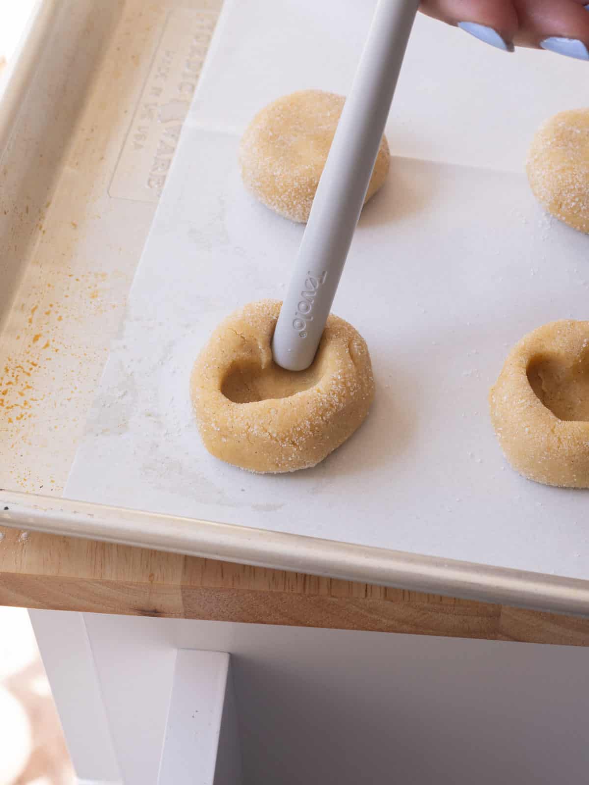 Using the end of a silicone spatula to create heart indents in cookie dough balls.