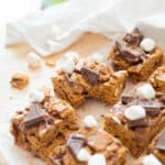 Golden graham bars on parchment paper on a wooden backdrop, surrounded by scattered marshmallows and graham crackers.