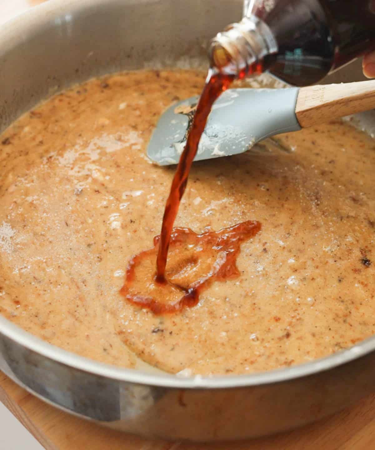 Pouring vanilla extract into large saucepan with melted brown butter and marshmallow mixture.