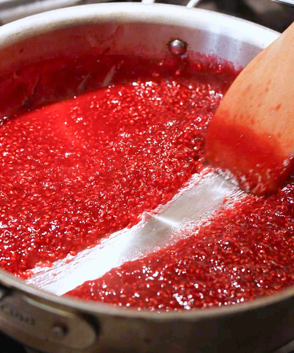 Using a wooden spatula to test if raspberry jam is done by seeing if it passed the streak test in the saucepan; it did pass!