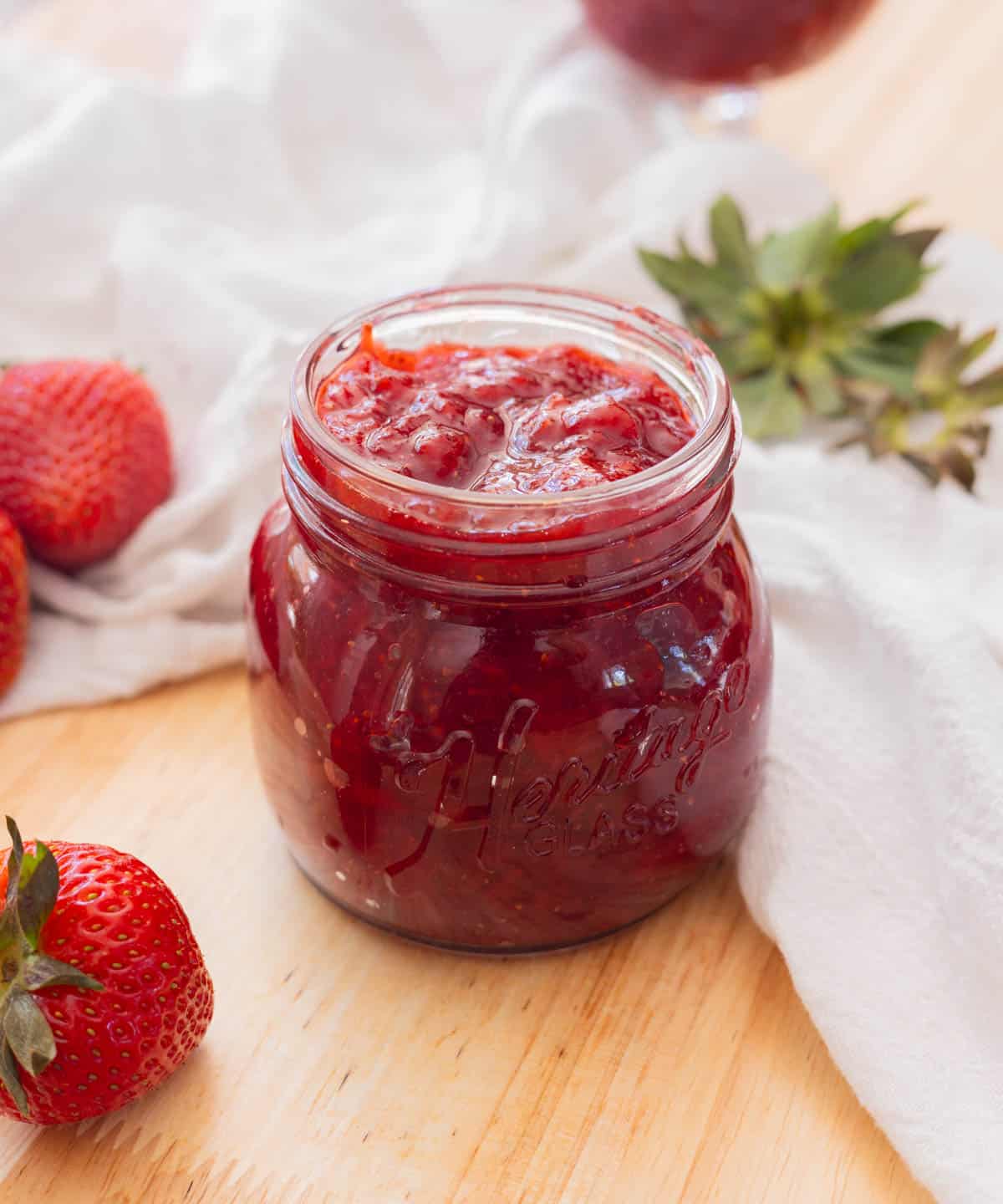 Delicious red strawberry jam in a glass jar on a wooden backdrop.