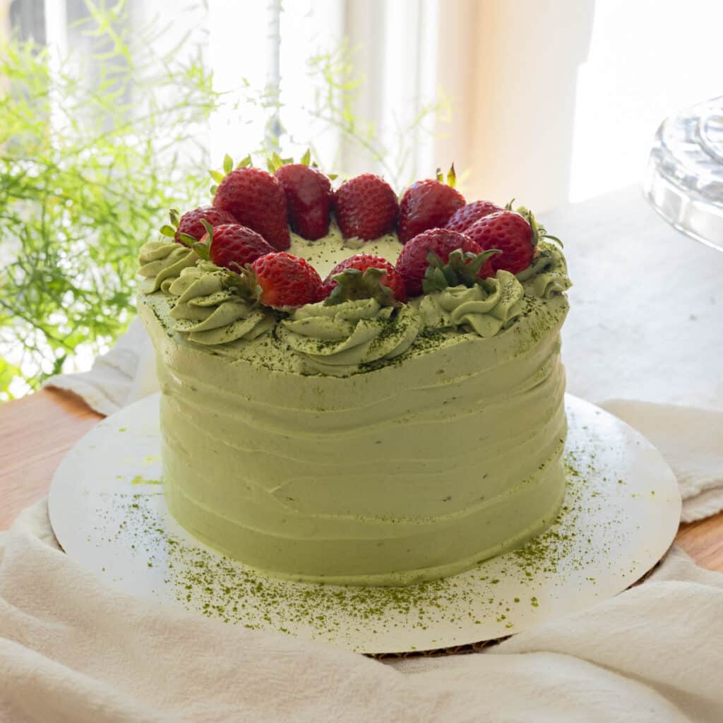 Slice of strawberry matcha cake on a fluted plate, with full cake in the background.