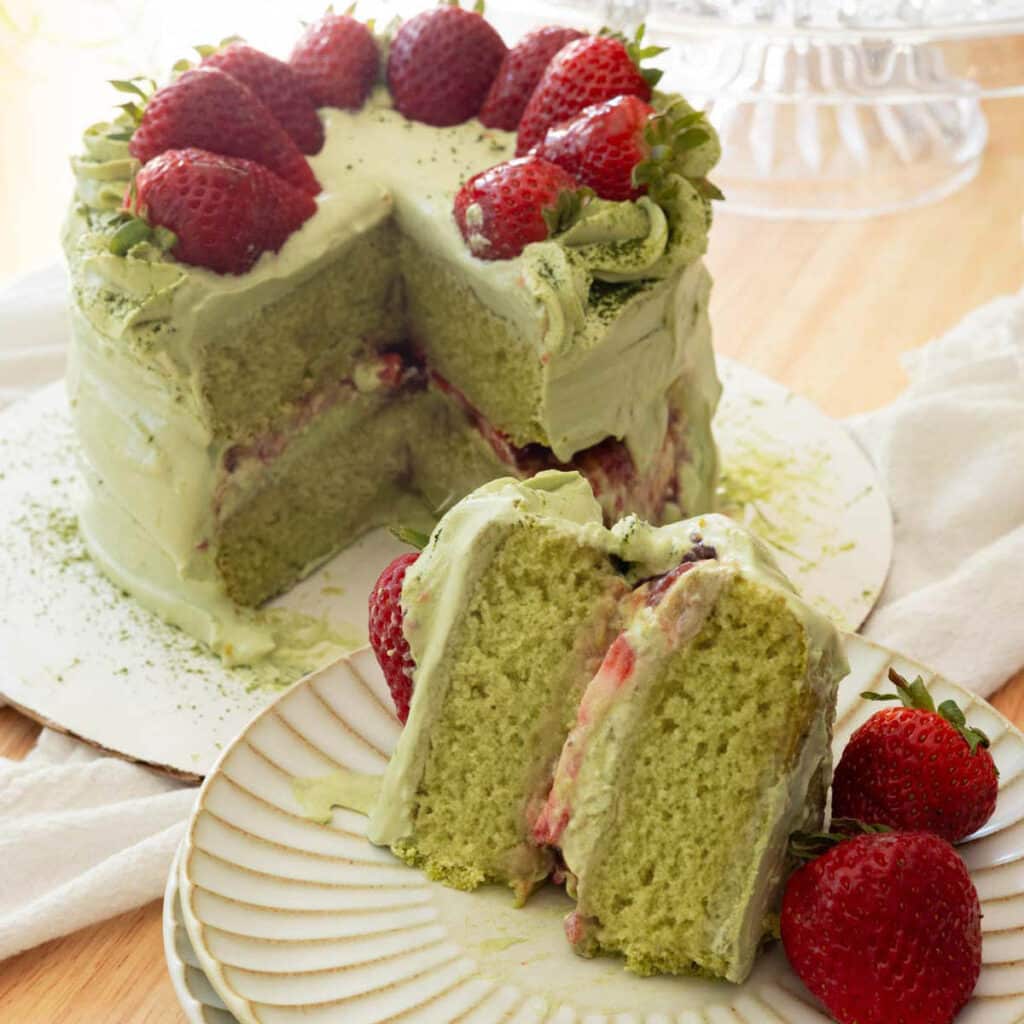 Slice of strawberry matcha cake on a fluted plate, with full cake in the background.