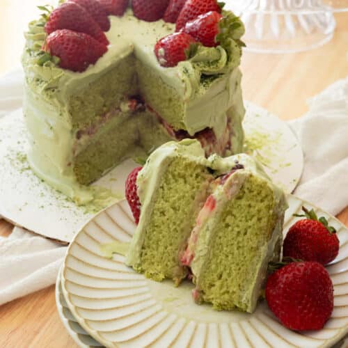 Slice of strawberry matcha cake on a fluted plate, with full cake in the background.