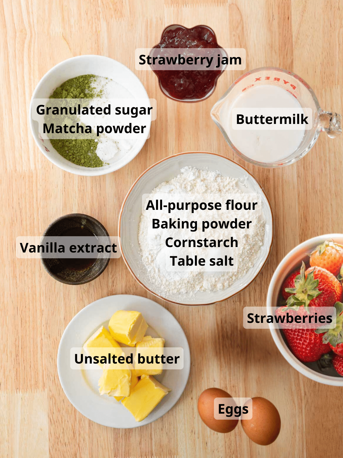 Matcha cake ingredients on a wooden backdrop with labels.