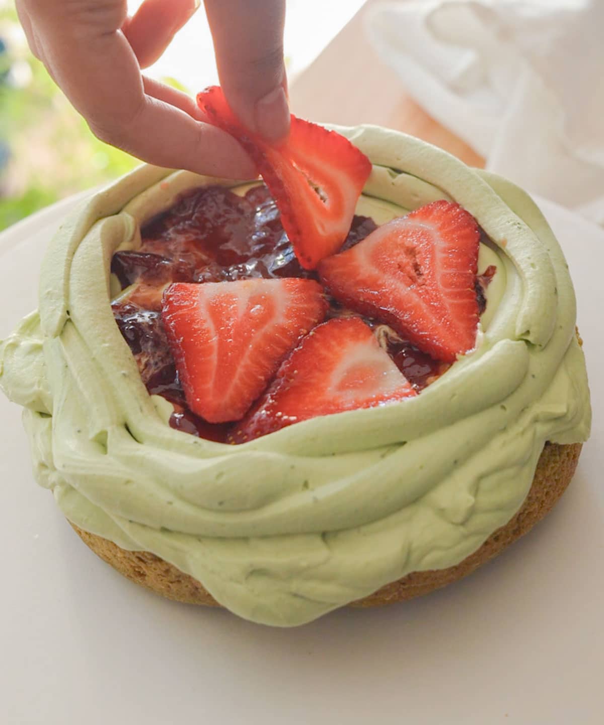 Topping first matcha cake layer with strawberry jam and strawberries.