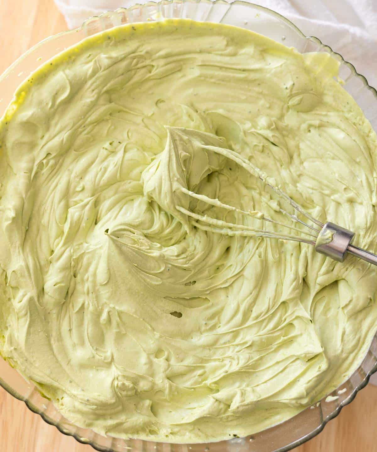 Matcha whipped cream with stiff peaks in a glass mixing bowl.