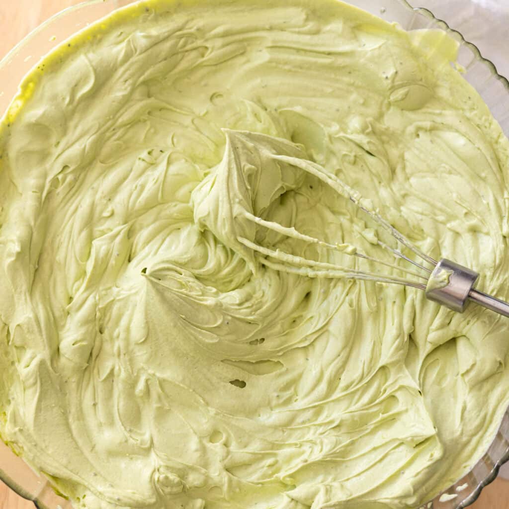 Matcha whipped cream with stiff peaks in a glass mixing bowl.