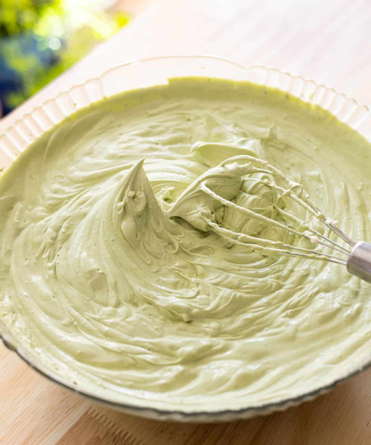 Stabilized matcha whipped cream with stiff peaks in a glass mixing bowl.