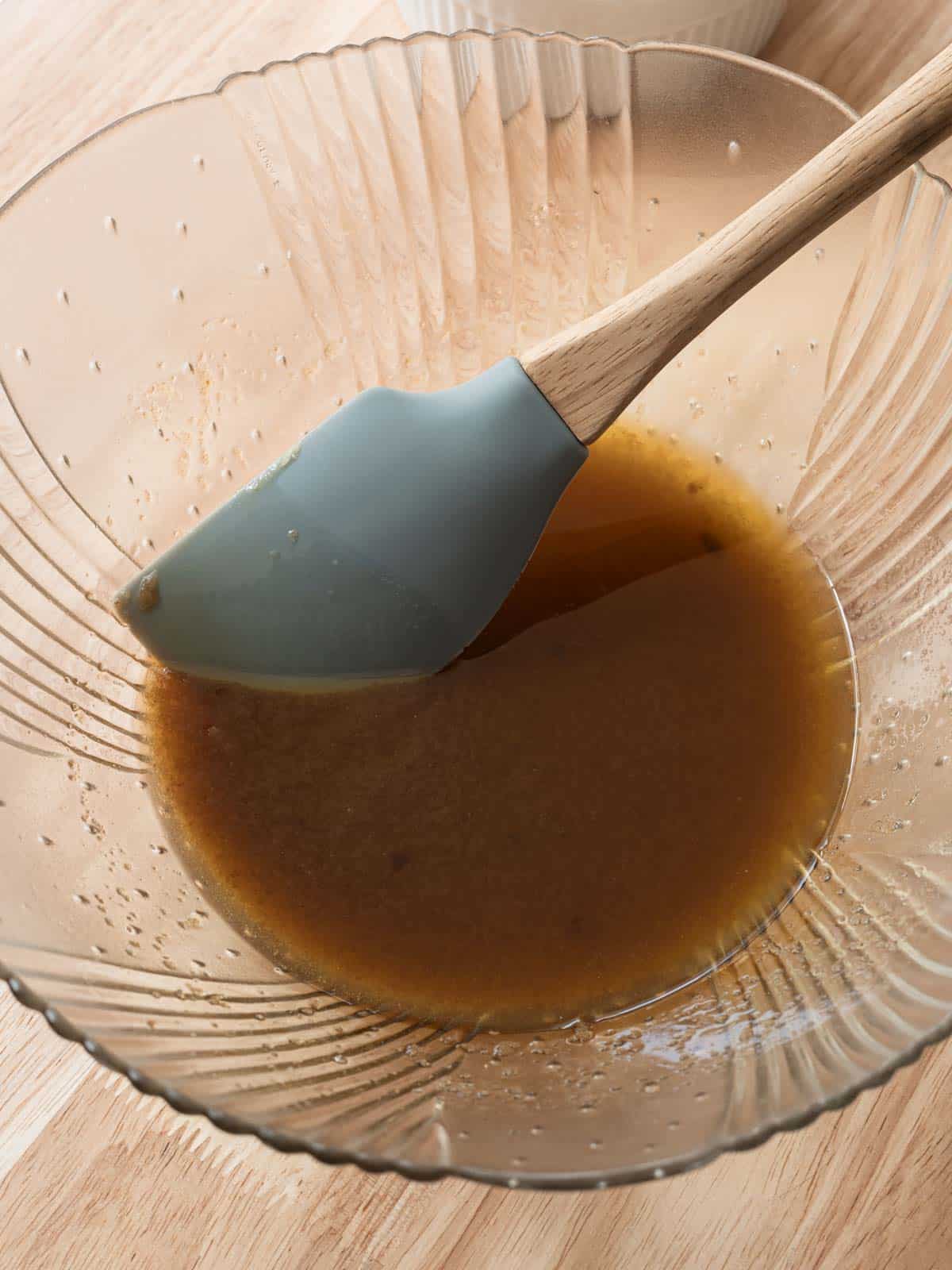 Mixed butter and sugars in a glass bowl with a silicone spatula.