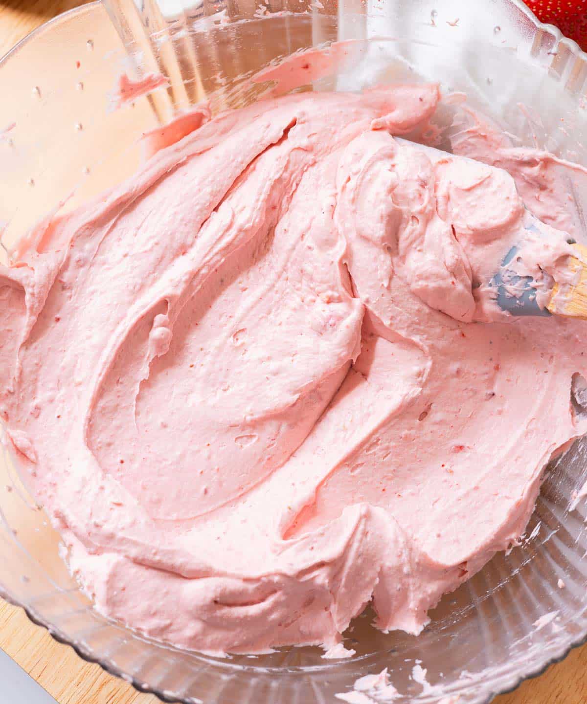 Fluffy, pink strawberry whipped cream frosting in glass mixing bowl.