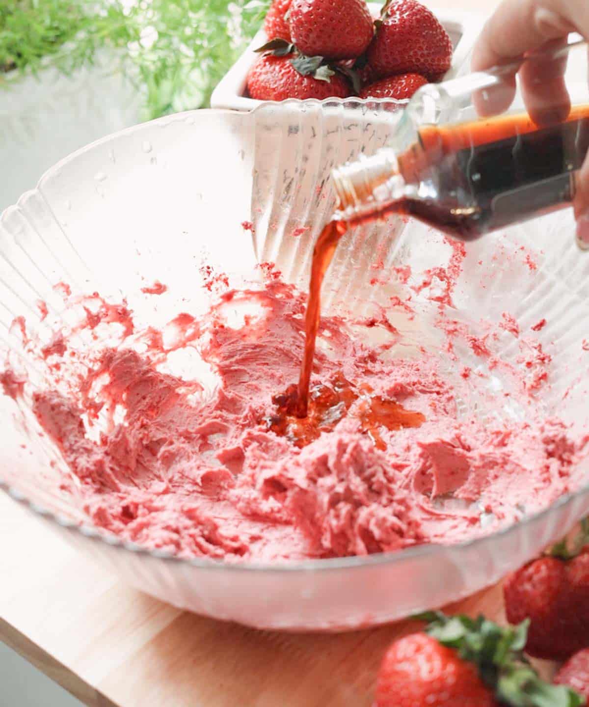 Pouring vanilla into a glass mixing bowl with whipped strawberry cream cheese.