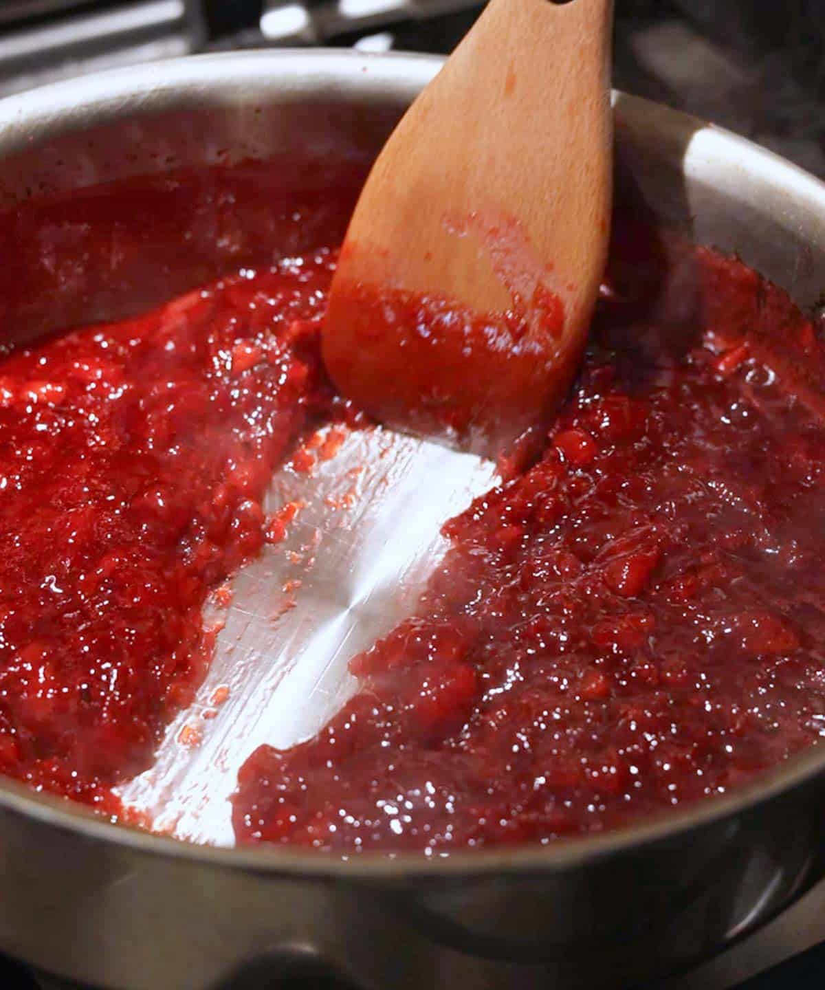 Using a wooden spatula to test if strawberry jam is done by seeing if it passed the streak test in the saucepan; it did pass!