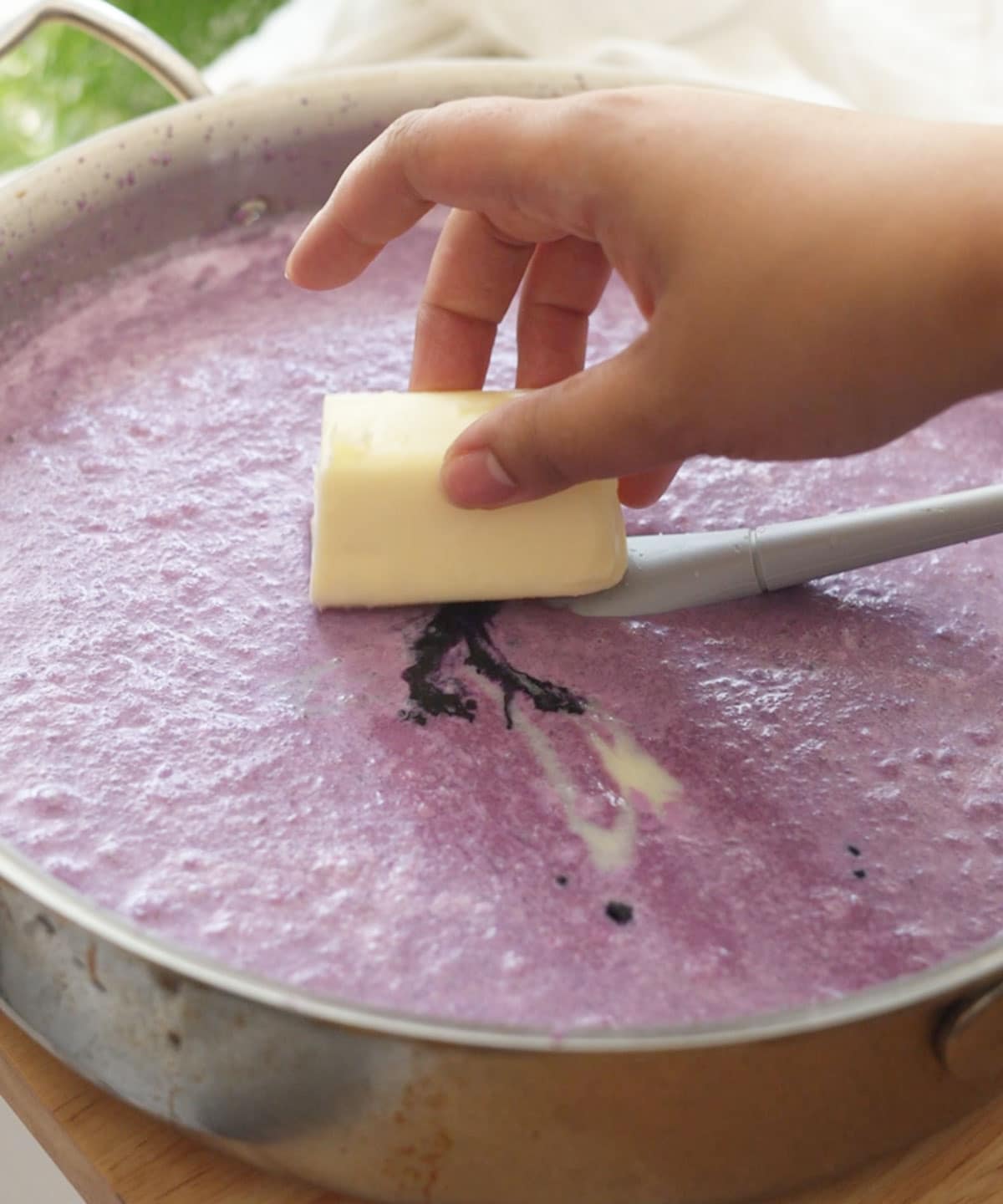 Adding half a stick of butter to pot with other ube halaya ingredients in it.