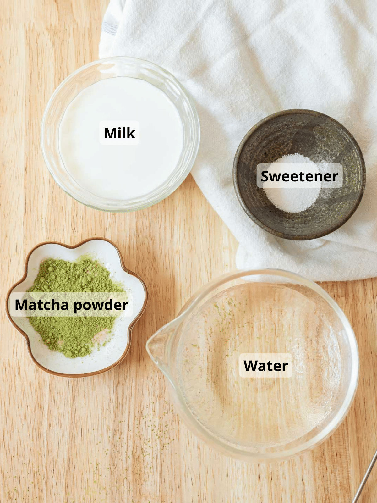 Matcha latte ingredients laid out on a wooden table, with labels for each ingredient.