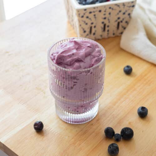 Blueberry cold foam in a fluted glass cup, on a wooden table.