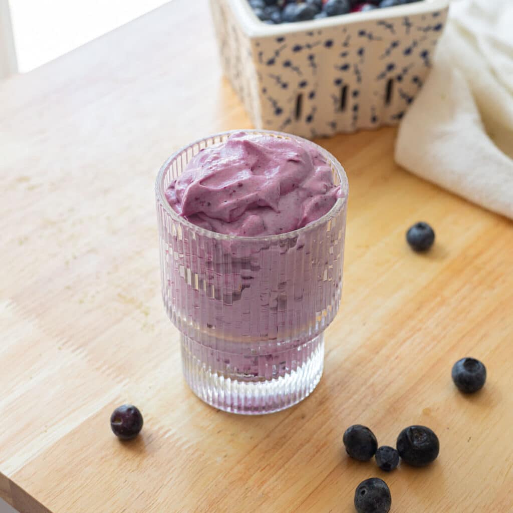 Blueberry cold foam in a fluted glass cup, on a wooden table.