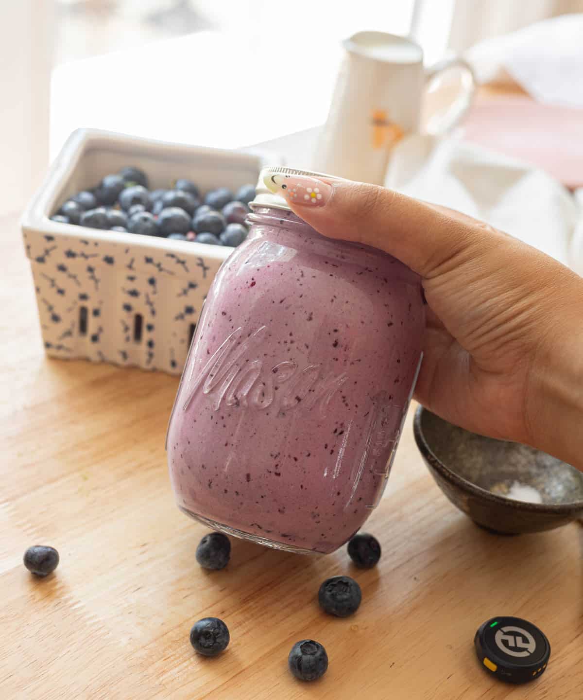 Holding a mason jar of already made blueberry cream cold foam.