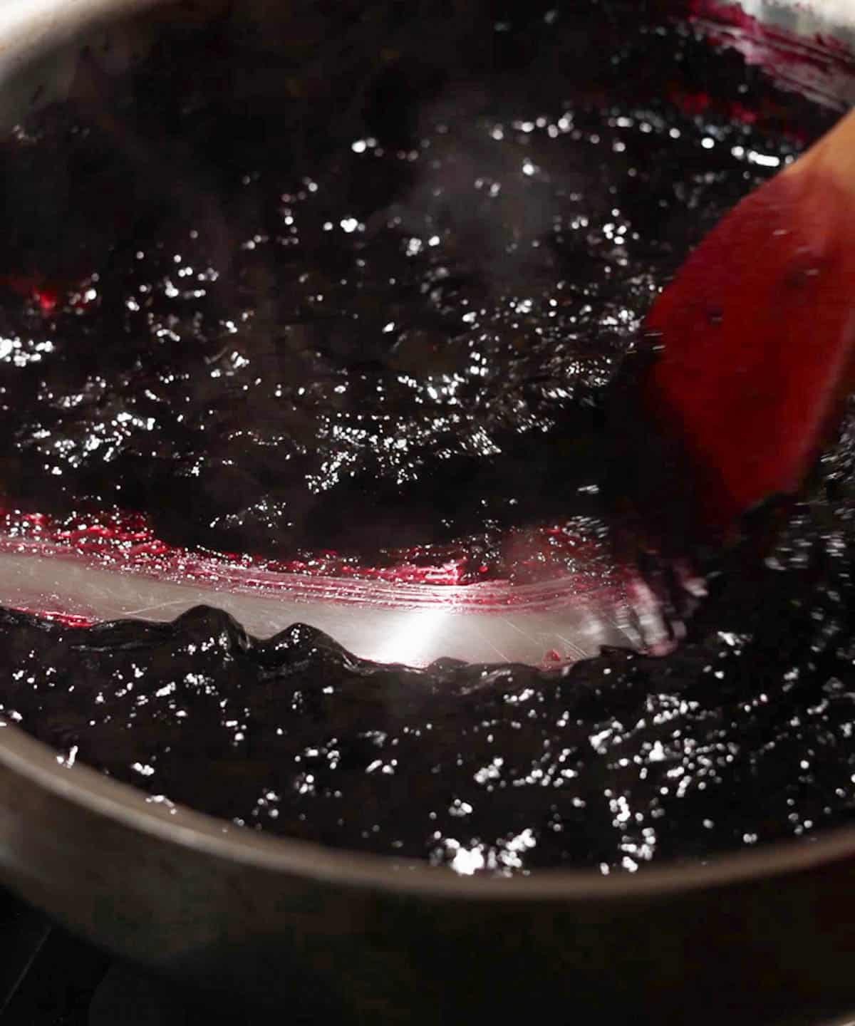 Using a wooden spatula to test if blueberry jam is done by seeing if it passed the streak test in the saucepan; it did pass!