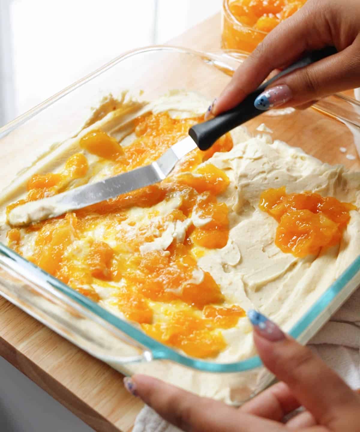 Using an offset spatula to spread homemade mango jam on top of mango whipped cream layer.