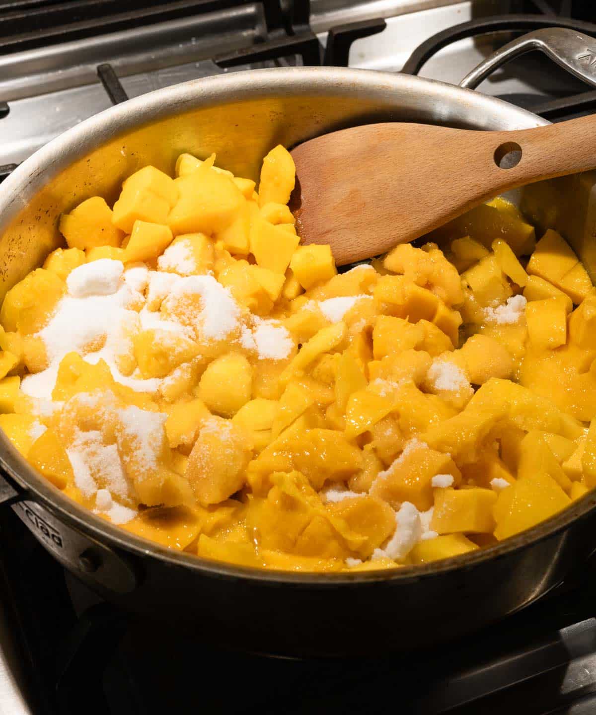 Large saucepan with roughly diced mangoes, granulated sugar, honey, lemon juice, and lemon zest.