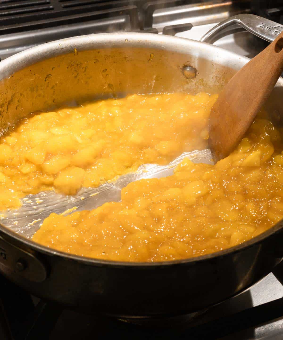 Using a wooden spatula to test if mango jam is done by seeing if it passed the streak test in the saucepan; it did pass!