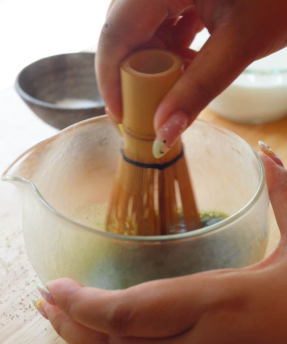 Using a bamboo whisk to whisk matcha powder and hot water in glass bowl.