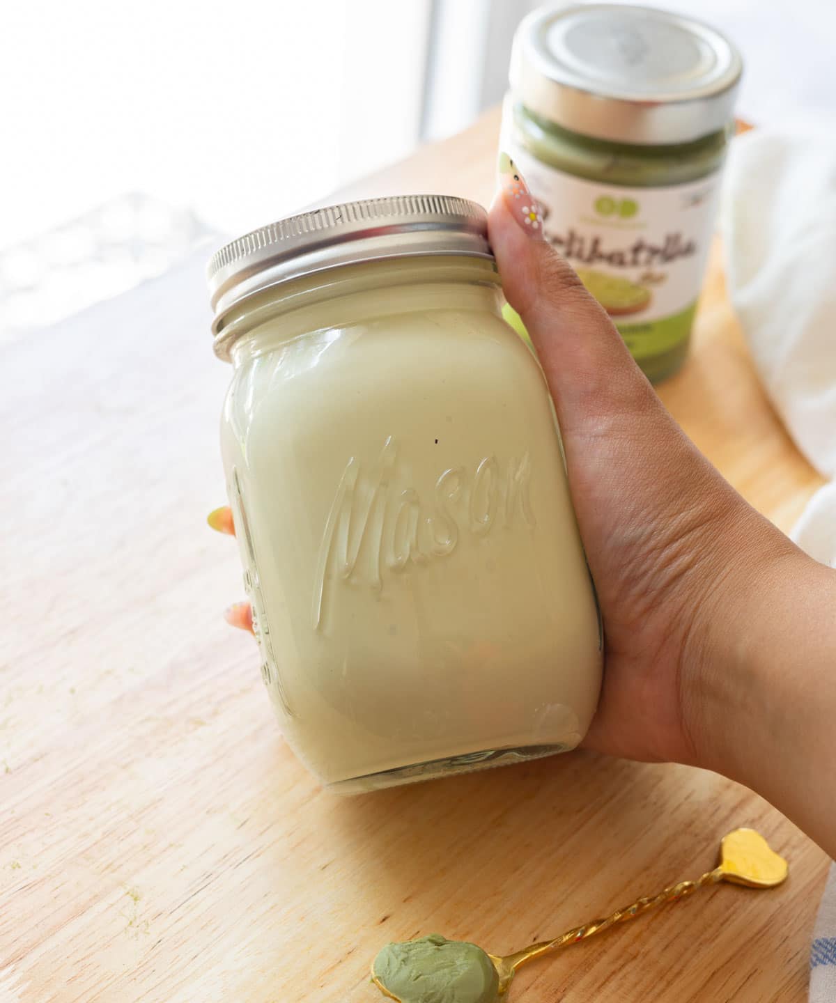 Holding a mason jar of already made pistachio cold foam.