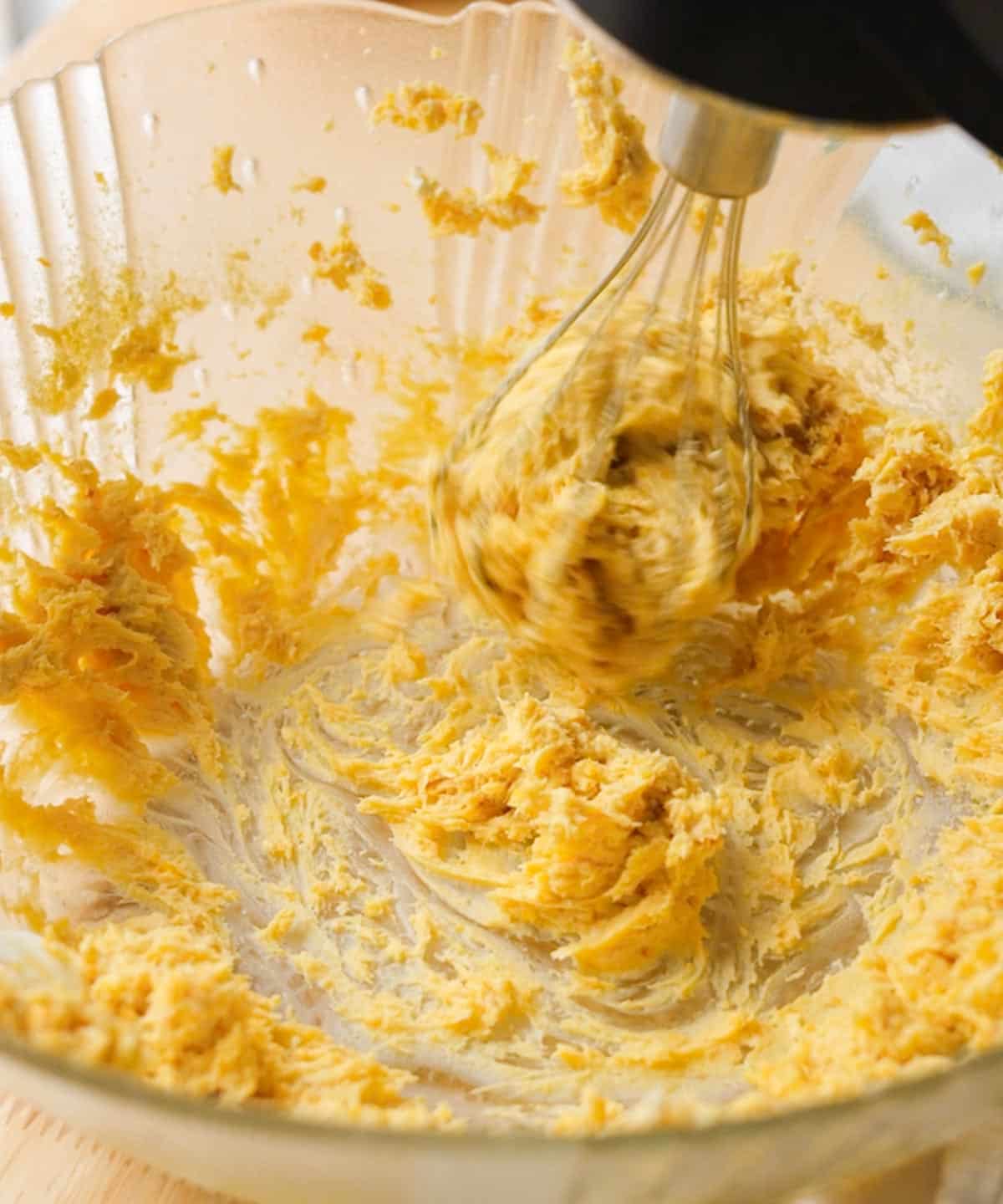 Using an electric mixer in a glass mixing bowl with whipped mango cream cheese.