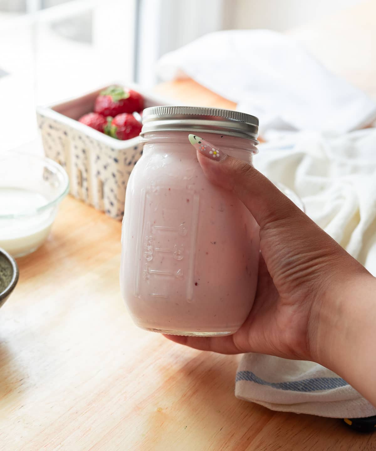 Holding a mason jar of already made strawberry cold foam.