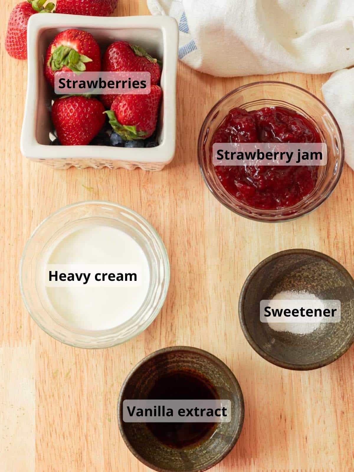 Strawberry cold foam ingredients laid out on a wooden table, with labels for each ingredient.