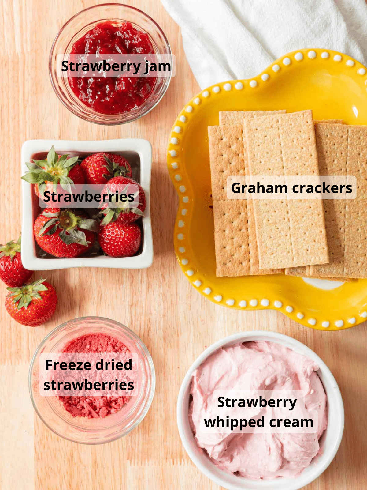 Strawberry icebox cake ingredients laid out on a wooden table, with labels for each ingredient.