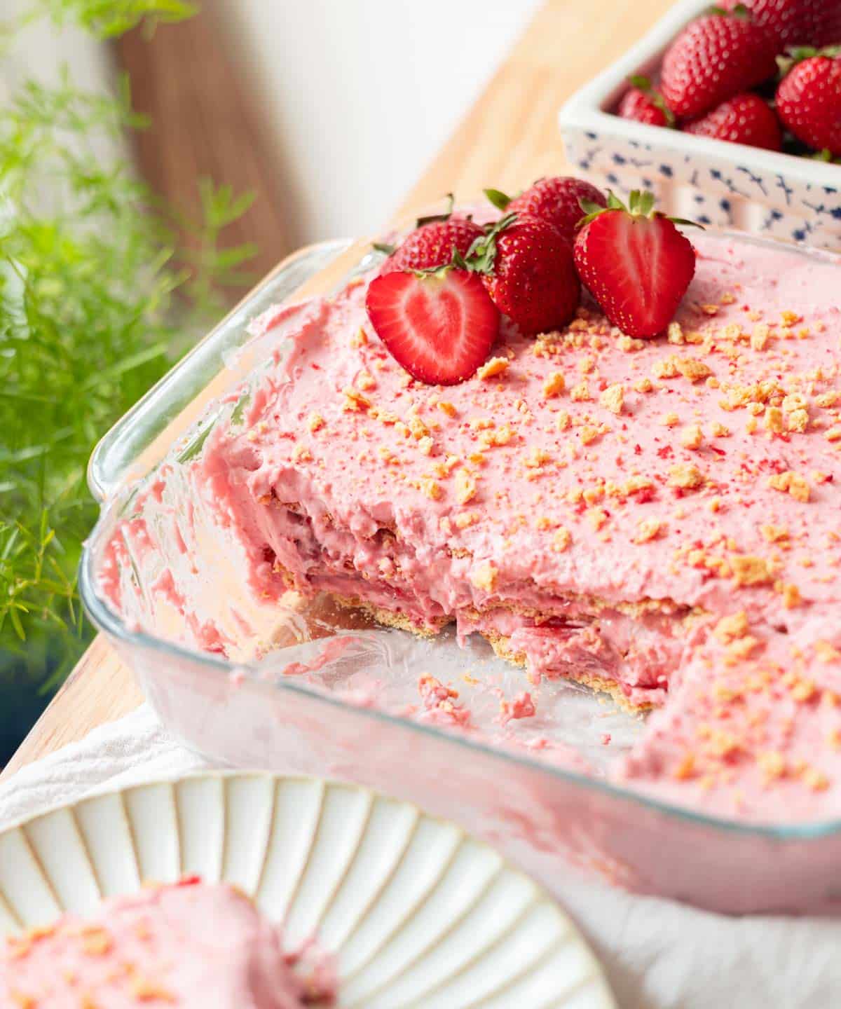 Strawberry icebox cake in glass baking dish with a large slice taken out of it.