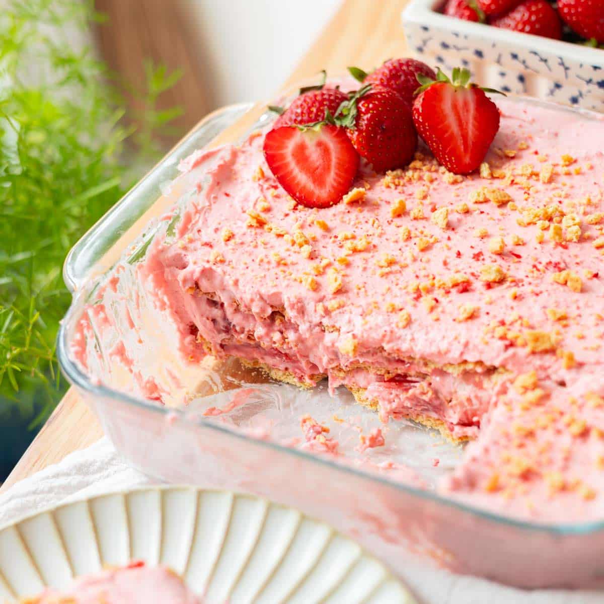 Strawberry icebox cake in glass baking dish with a large slice taken out of it.