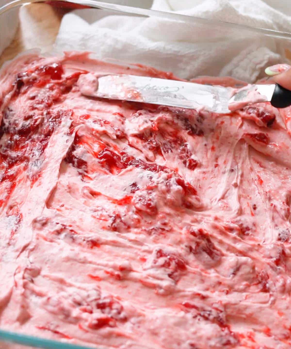 Using an offset spatula to spread strawberry jam on top of strawberry whipped cream layer.