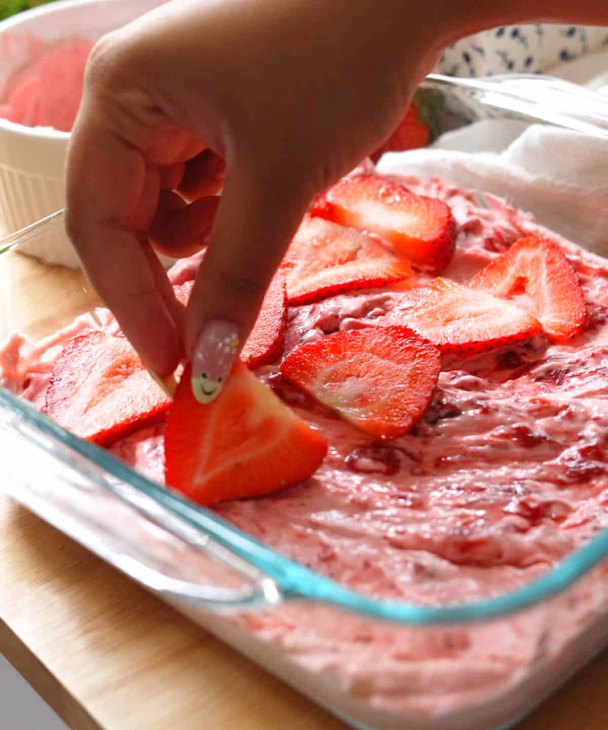 Adding thin slices of strawberries on top of strawberry jam layer.